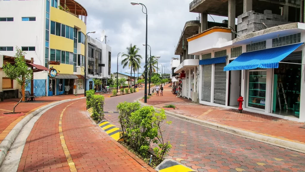 Street view of Puerto Ayora, the largest town in the Galápagos Islands, with shops, trees, and people walking.
