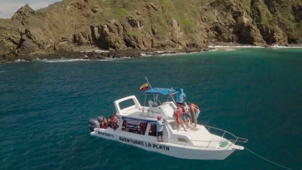 White boat named “AVENTURAS LA PLATA” with passengers sailing near the rocky shores of Isla de la Plata, Ecuador.